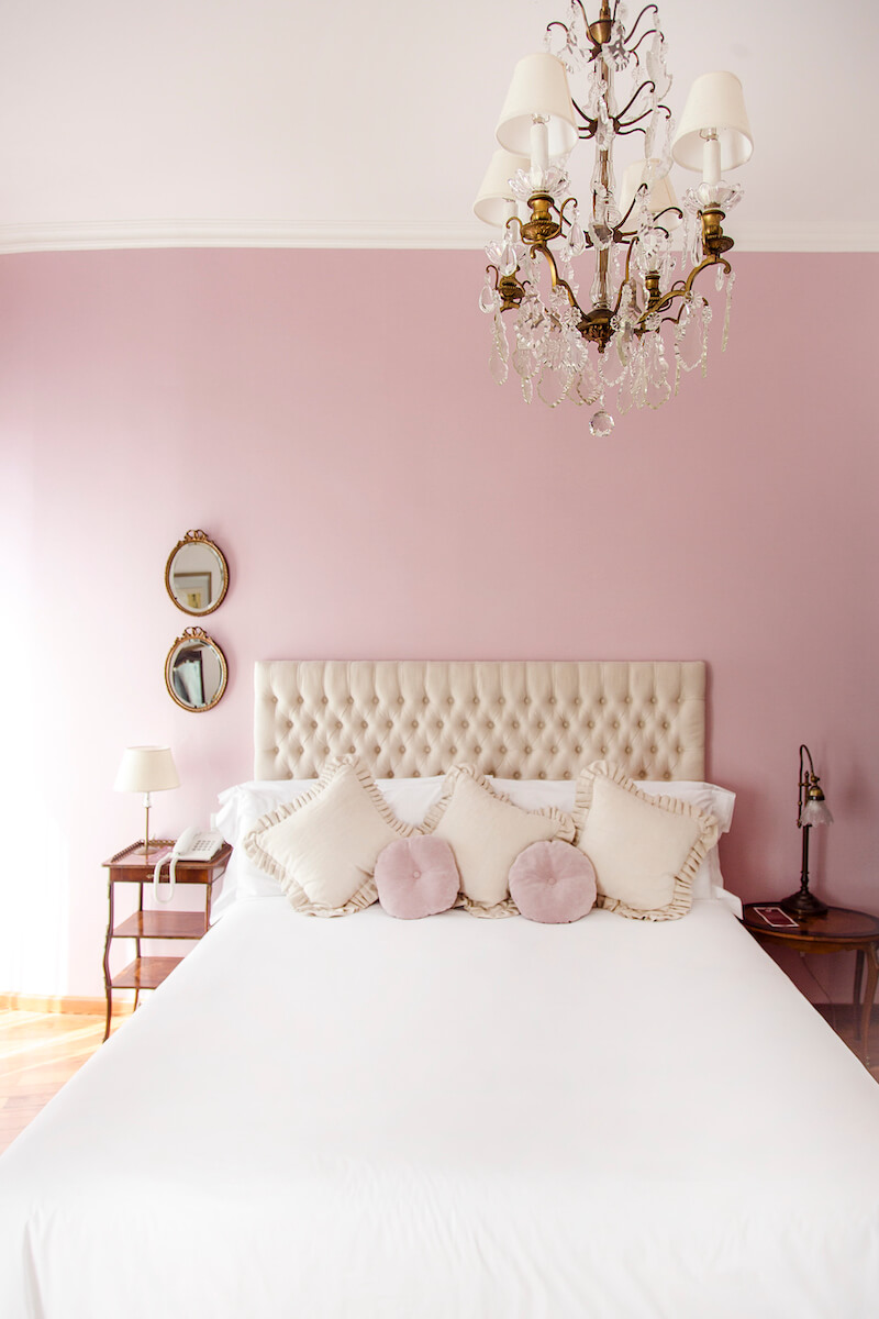 A pink-walled bedroom with a large white bed and a glass chandelier