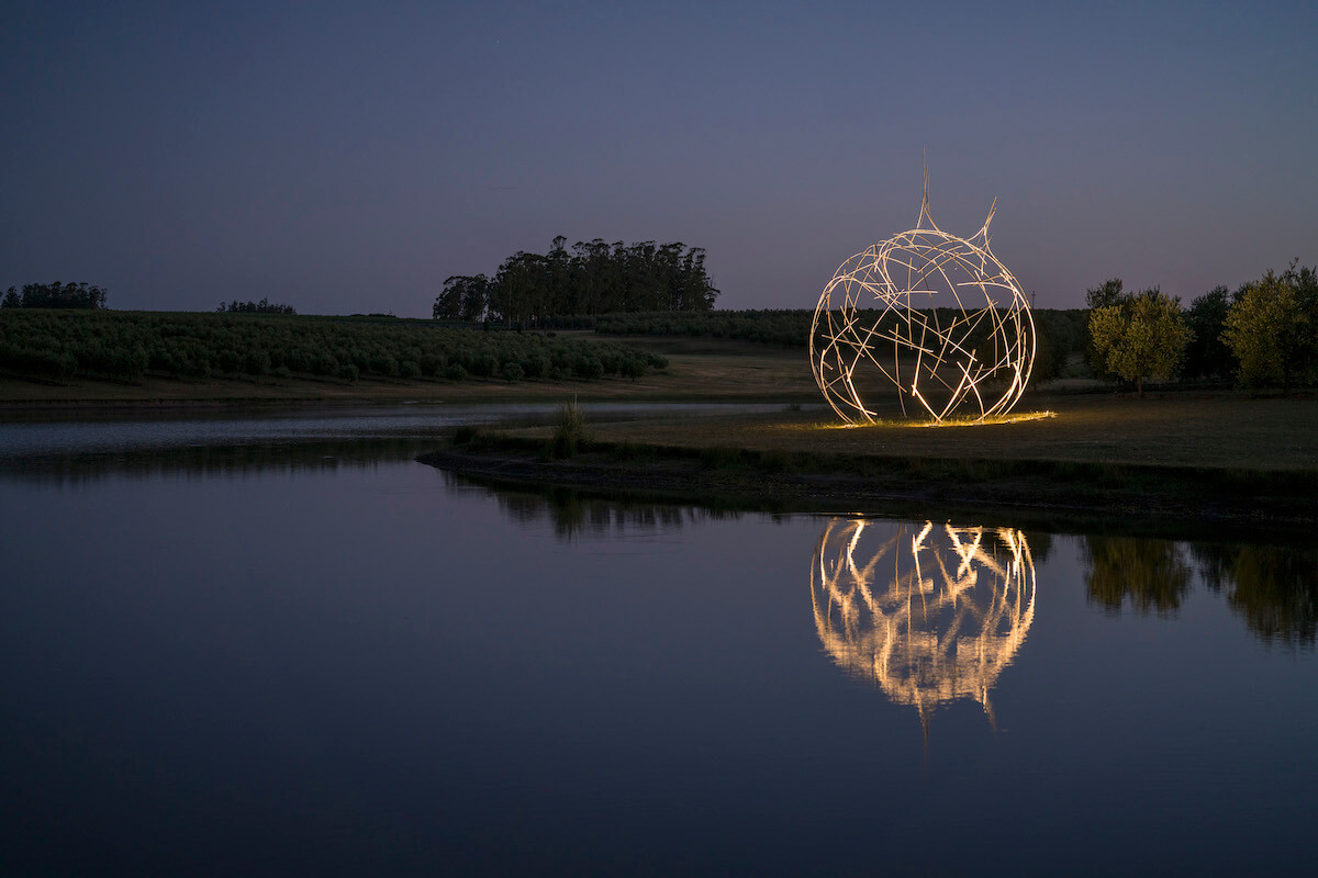 A stainless steel sphere illuminated at night by a lake, a piece of art called Semilla Estelar, by the Uruguayan artist Diego Santurio.