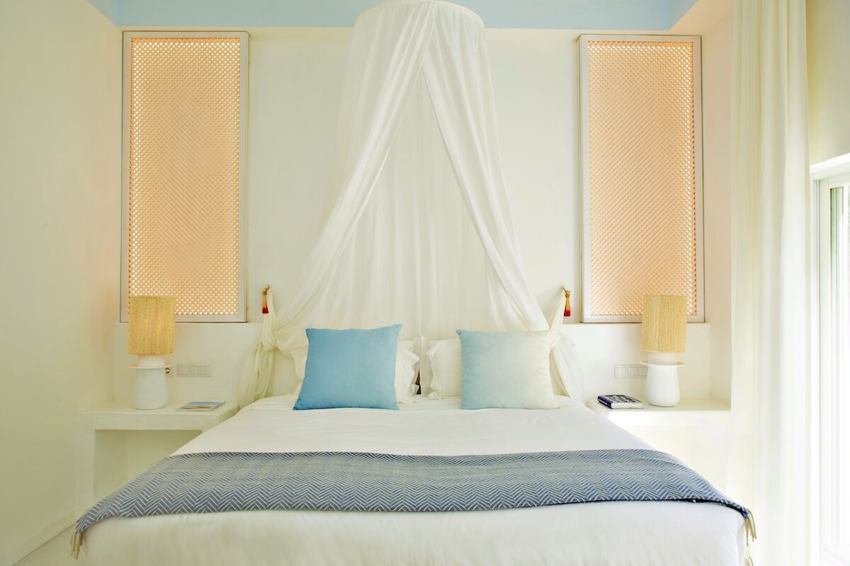 A light and airy room with white walls and a large canopied bed in the center at the Ocean and Mountain View Suite