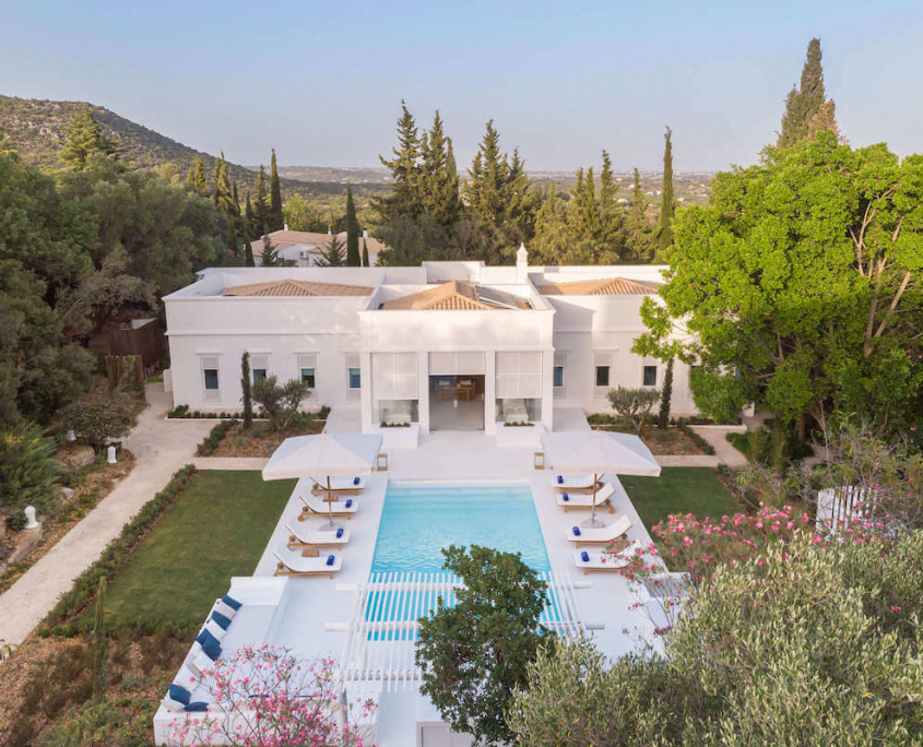 An aerial view of the exclusive Villa Indigo and its large turquoise pool with sun loungers and green trees on either side