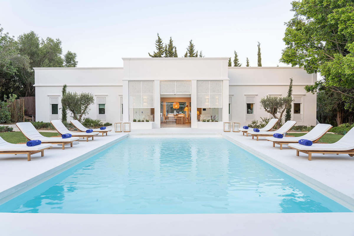 A turquoise pool with white sun loungers on either side leading to a private terrace at the exclusive Villa Indigo