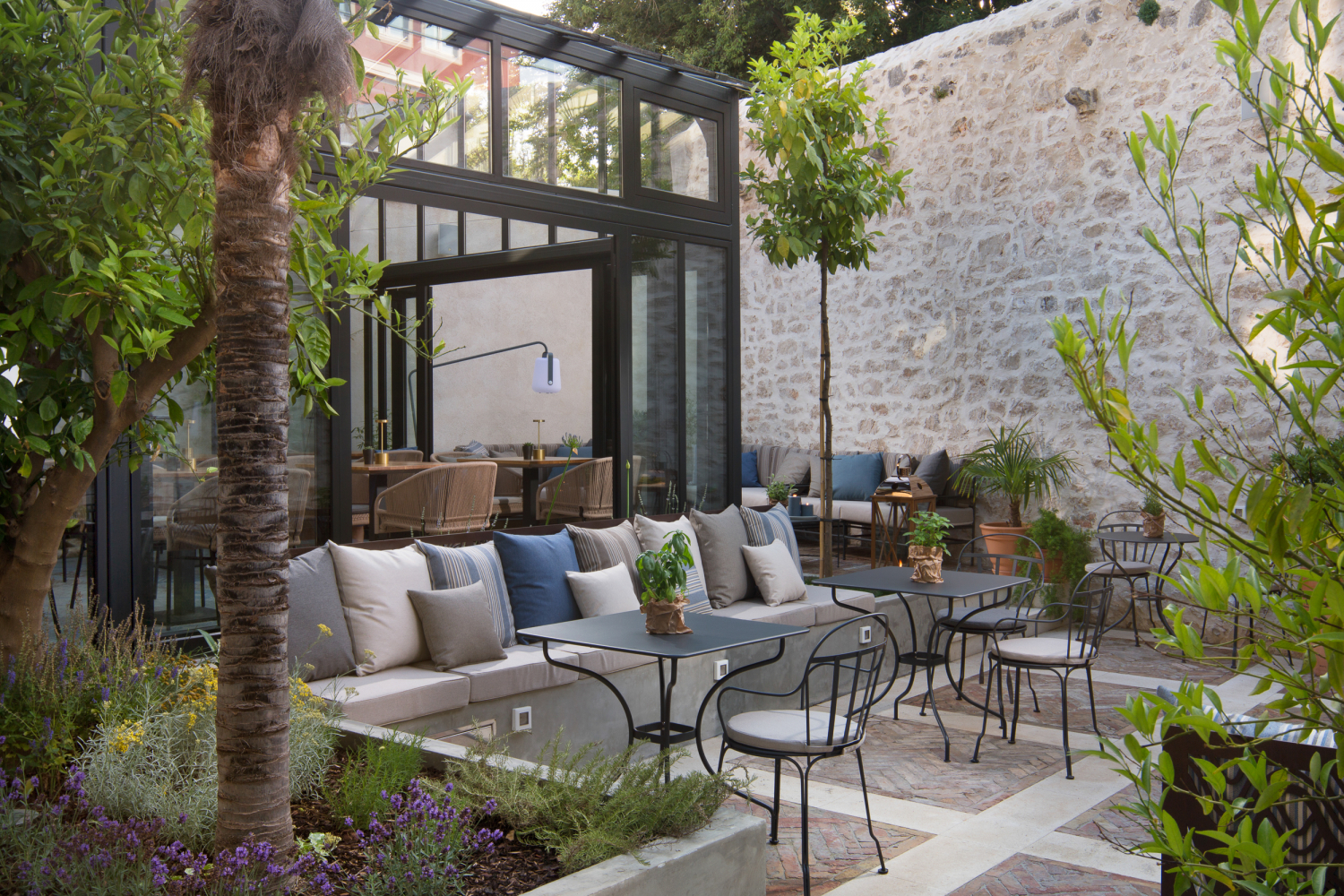 An inner walled courtyard with lots of green plants and tables and chairs for guest to dine