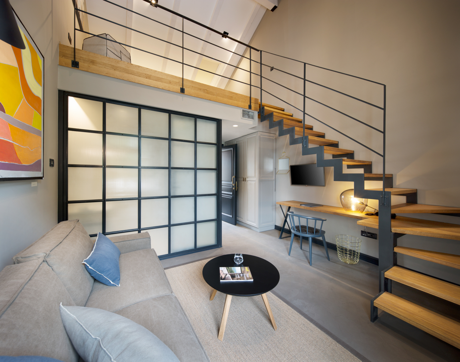 A room with a grey sofa and a wood and steel staircase leading up to a second mezzanine level