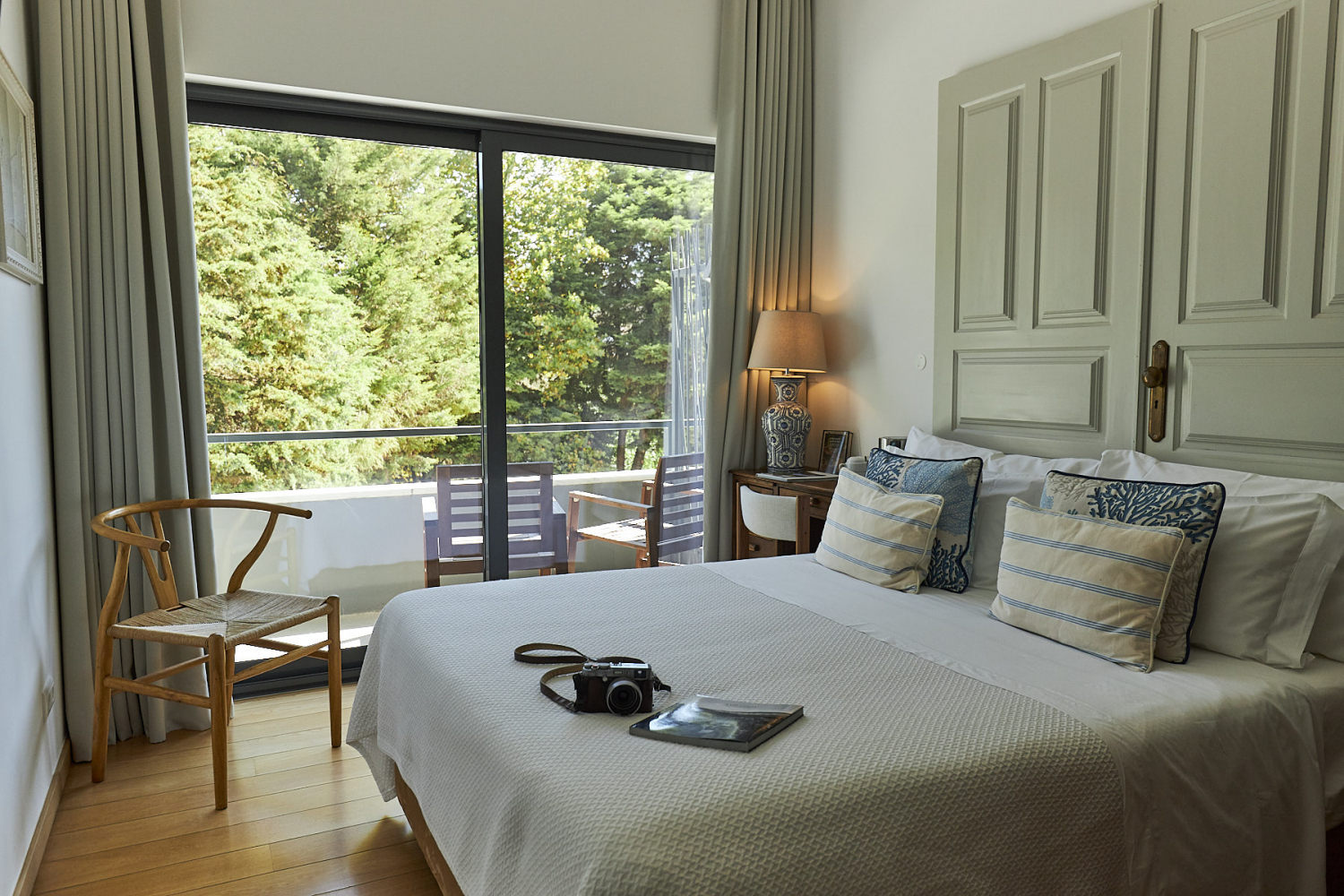 A comfortable room with a double bed and large french doors opening onto a view of lush green trees